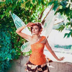 a woman dressed in an orange top and patterned skirt is holding a green fairy wings