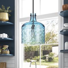 a blue glass light hanging from a kitchen window over a sink and counter top next to open shelves