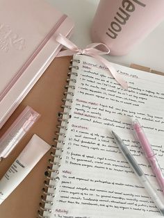 an open notebook with pink writing on it next to two pens and a coffee mug