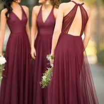 two bridesmaids in maroon dresses are looking at each other with their backs to the camera