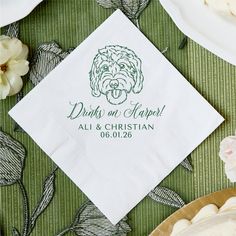 a white napkin with a dog on it sitting next to some plates and flowers in the background