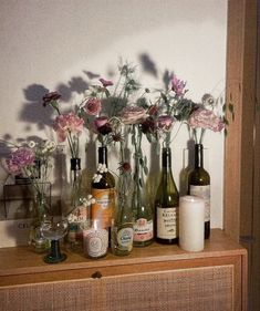 flowers in vases and bottles on top of a wooden shelf next to a wall