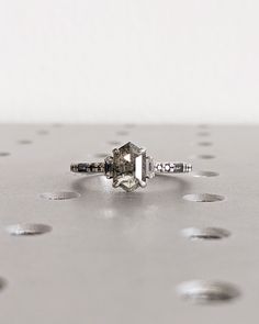 a diamond ring sitting on top of a silver surface with dots around it and the center stone is surrounded by smaller round holes