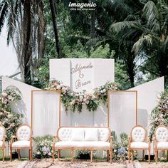 an outdoor wedding setup with white couches and greenery on the wall behind them