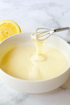 a whisk in a white bowl next to a lemon slice and a mixer