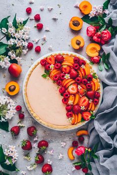 a pie topped with sliced peaches and strawberries on top of a white table