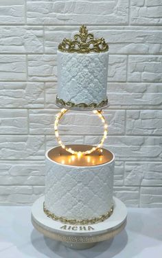 a three tiered white cake with gold decorations and lights on the top is sitting on a pedestal