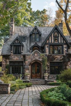 a large stone house with lots of windows and plants on the front lawn, surrounded by greenery