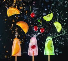 popsicles with fruit and water splashing out of them on a black background,