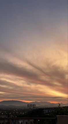 the sun is setting behind some clouds in the sky over a city with mountains and buildings