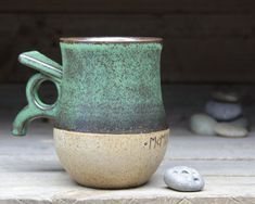 a green and white coffee cup sitting on top of a table next to a rock