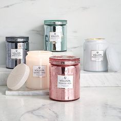 three different types of candles sitting on a marble counter top next to each other,