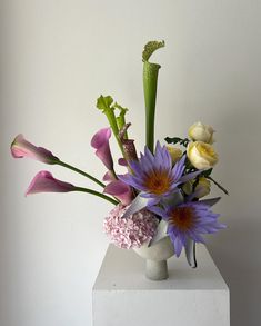 a vase filled with purple and yellow flowers on top of a white pedestal next to a wall