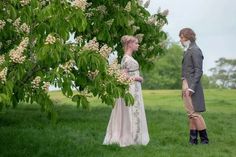 two people standing in the grass under a tree