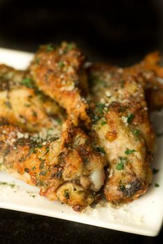 chicken wings covered in parmesan cheese and herbs on a white plate with black background