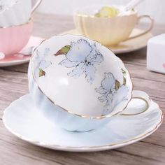 three tea cups and saucers with flowers on them sitting on a wooden table top