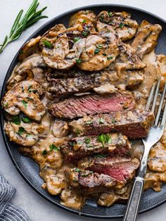 steak with mushroom gravy and mushrooms on a black plate next to a fork