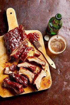 ribs covered in bbq sauce on a cutting board next to a glass of beer