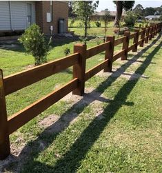 a wooden fence in front of a house with grass on the ground and trees behind it