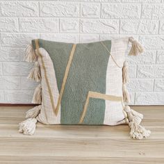 a green and white pillow with tassels on the bottom, sitting against a brick wall