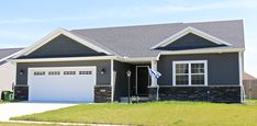 a gray house with two garages and a flag in the front yard on a sunny day