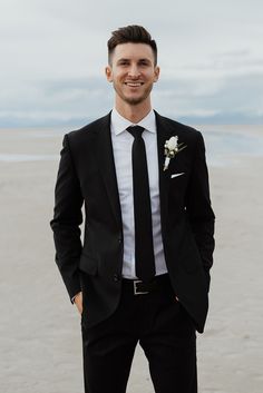 a man in a suit and tie standing on the beach