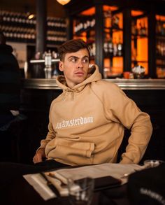 a man sitting at a table in front of a bar wearing a brown hoodie