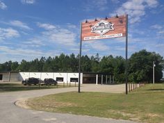 the sign is in front of an empty parking lot with cars parked outside and trees behind it