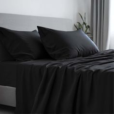 a bed with black sheets and pillows in a room next to a potted plant