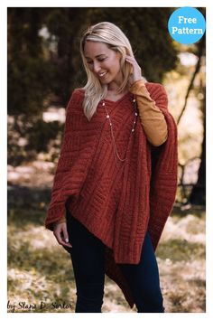 a woman wearing a red sweater and black jeans standing in the woods with her hand on her head