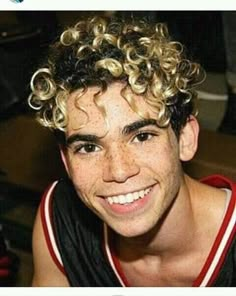 a young man with curly hair smiling at the camera while wearing a red and black tank top