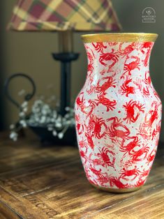 a red and white vase sitting on top of a wooden table next to a lamp