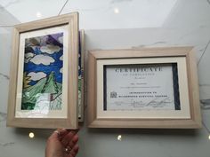 a person holding up a certificate in front of two framed pictures