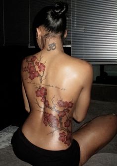 a woman is sitting on the floor with her back turned to the camera and tattoos on her body