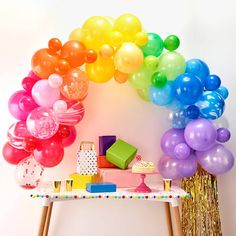 a table topped with lots of balloons next to a rainbow shaped arch on top of a wall