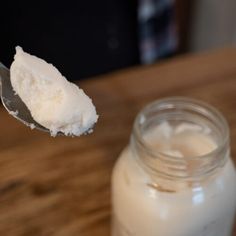 a spoon full of white sugar sitting next to a jar on a wooden counter top