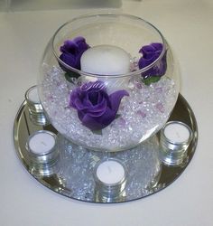 a glass bowl filled with water and purple flowers on top of a silver platter