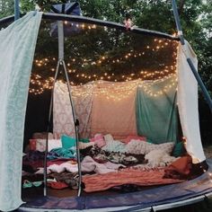 an outdoor tent is set up with clothes and lights on the trees in the background