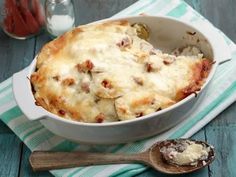 a casserole dish with meat and cheese in it next to a wooden spoon