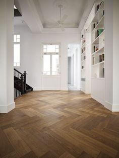 an empty room with wood flooring and white bookshelves on the wall, in front of a staircase