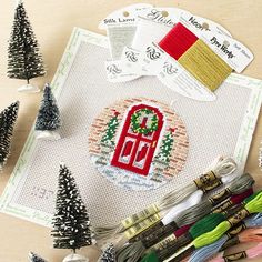 the cross stitch pattern is next to some christmas trees and other crafting supplies on a table