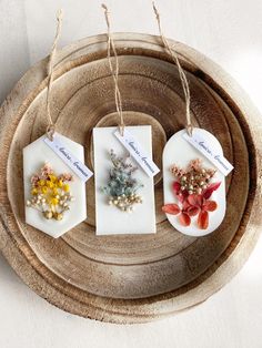 three small tags with flowers on them are hanging from twine strings in front of a wooden tray