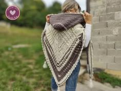 a woman is holding up a shawl in front of a brick wall and grass