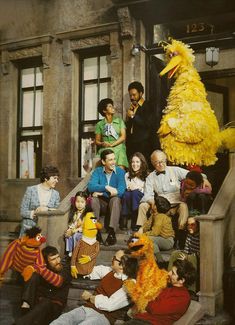 a group of people sitting on the steps in front of a building with a large yellow bird