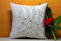 a red rose sitting next to a white pillow with sequins and beads on it