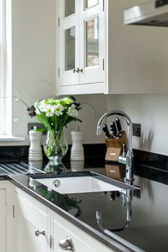 a kitchen sink sitting under a window next to a vase with flowers