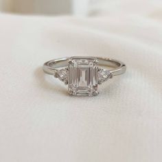 an emerald - cut diamond ring sits on a white cloth