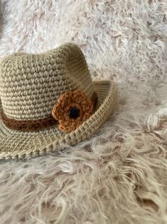 a crocheted hat with a brown flower on the brim sits on fluffy white fur