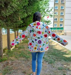 a woman walking down a dirt road with her arms spread out and flowers on the jacket