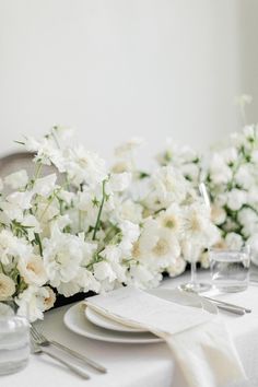 the table is set with white flowers and silverware